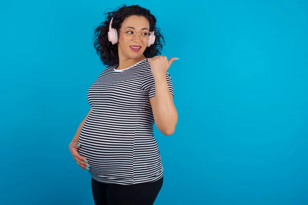 Gravid Arabisk Kvinne Iført Stripete Skjorte Lytter Lydspor Trådløse Hodetelefoner – stockfoto