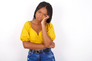 Çok sıkılmış bir Afro-Amerikan kadını sarı bluz giyer ve kot pantolon yanak yanağa tutuşurken diğer eli çaprazlanmış, yorgun ve hasta görünür..