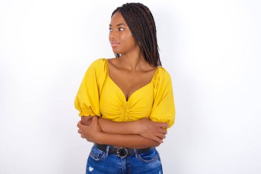 Sarı bluz giyen, kot pantolon giyen mutlu bir şekilde ellerini göğsünün üzerinde gezdiren mutlu genç bir kadın.