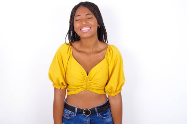 Pozitif, genç, güzel bir kadın, sarı bluz giyiyor, kot pantolon giyiyor, neşeli bir ifade takınıyor, gözlerini kapatıyor ve gülüyor. 