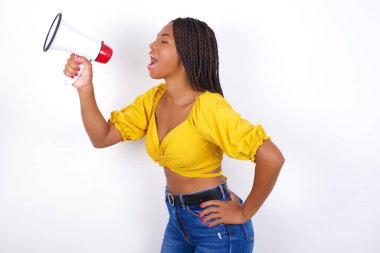 Sarı bluzlu ve kot pantolonlu komik genç bir kadın stüdyoda megafonla bağırıyor.