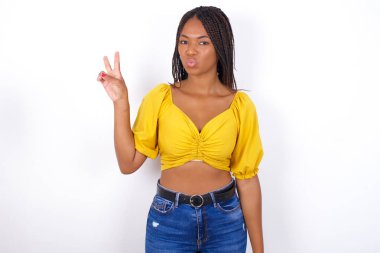 Sarı bluz giyen genç ve güzel bir kadın barış jesti yapıyor dudakları katlanmış V işaretini koruyor. Vücut dili kavramı