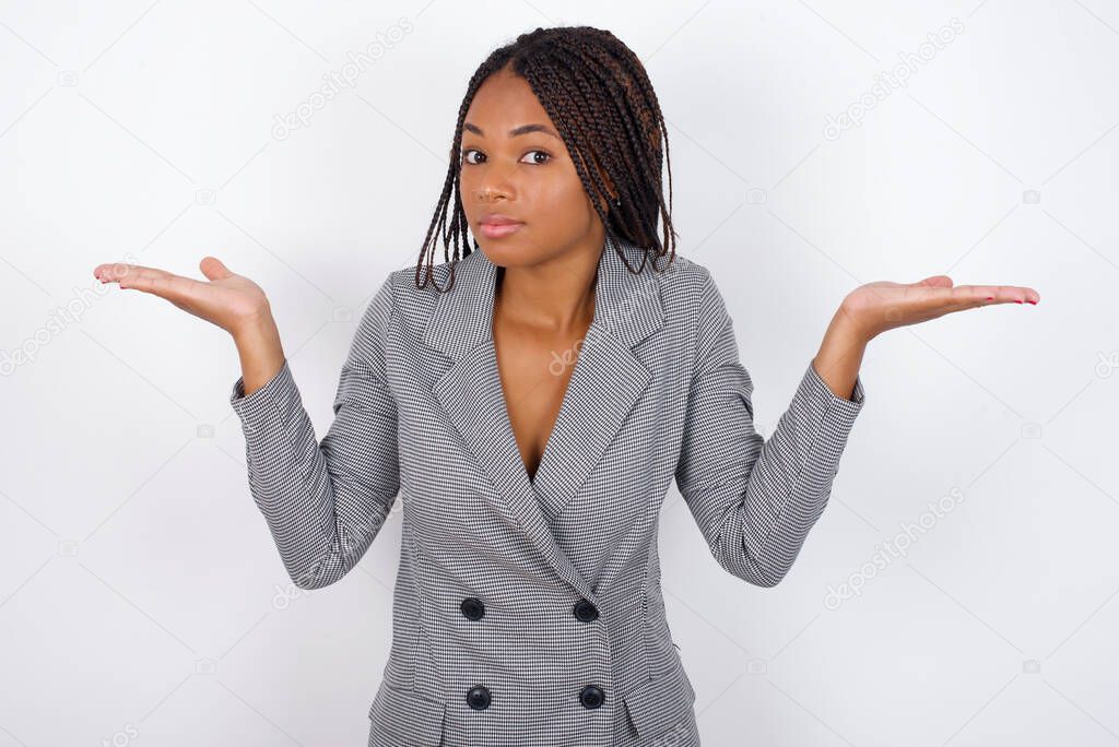 Puzzled and clueless  young beautiful african american businesswoman  with arms out, shrugging shoulders, saying: who cares, so what, I don't know.