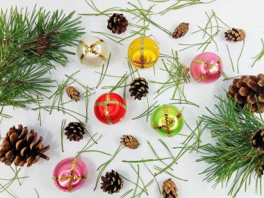 Renkli Noel süsleri ve çam kozalakları beyaz arka planda dağınık çam iğneleriyle sıralanmış. Minimum festival dairesi kış tatillerini, Noel 'i ve yeni yıl kutlamalarını simgeliyor. Mevsimlik arka planlar için mükemmel