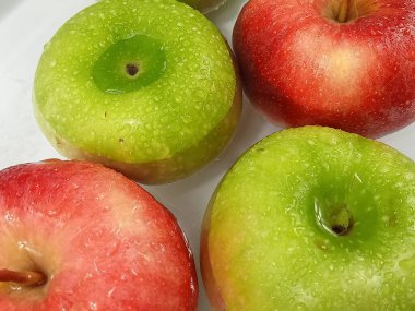 Temiz beyaz zemin üzerinde su damlacıklarıyla kaplı taze kırmızı ve yeşil elmaların yakın plan görüntüsü. Canlı renkler, doğal nem ve taze meyve dokusu tazelik ve kaliteyi iletir. Bu da bu fotoğrafı sağlıklı temalar için mükemmel kılar. 