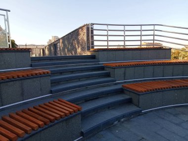 Kavisli taş basamakları ve ahşap oturma elementleri olan modern bir şehir merdiveni. Minimalist tasarım, temiz hatlar ve metal parmaklıklar çağdaş bir kamusal alan estetiği yaratır. Mimari ve şehir altyapısıyla ilgili konular için uygundur,