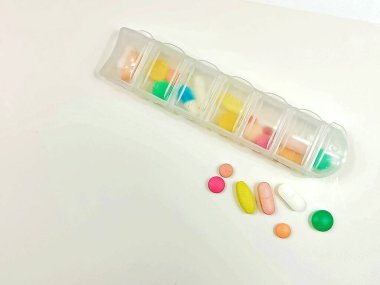 Temiz beyaz bir yüzeye yerleştirilmiş çeşitli vitamin ve ilaçlarla dolu saydam bir ilaç organizatörü. Bunun yanında çeşitli renkli tabletler ve kapsüller düzenlenerek açık bir tıbbi ve sağlıklı kompozisyon oluşturulur. Konular için uygun.
