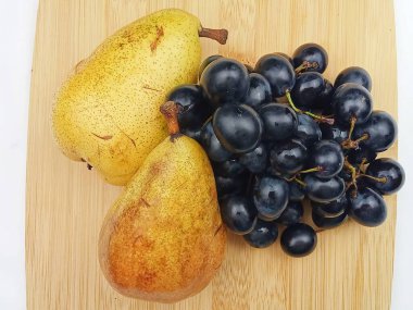 Taze armutlar ve açık tahta bir tahtanın üzerine yerleştirilmiş koyu üzümler. Sağlıklı yeme, organik üretim, mevsimlik meyve, beslenme, vejetaryen yaşam tarzı ve temiz minimalist yerleşim temaları için uygun doğal besin bileşimi.