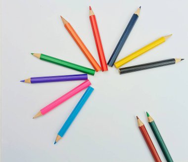 Parlak renkli kalemler, beyaz arka planda, yarı dairesel, yaratıcı bir düzende dizilmiş. Eğitim temaları, okul malzemeleri, yaratıcılık kavramları, tasarım planları ve tanıtım materyalleri için uygun asgari sanatsal kompozisyon.