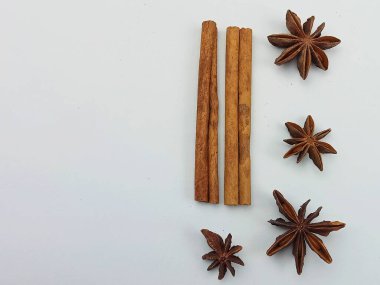 Minimalist tarçın çubukları ve yıldız anasonu bembeyaz arka planda dizilmiş. Sıcak kahverengi baharatlar yemek blogları, mutfak temaları, sonbahar ve kış tarifleri, tatil kavramları, aromatik baharatlar için mükemmel aromatik bir kompozisyon oluşturur.