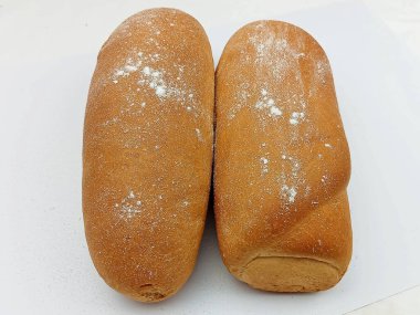 Temiz beyaz bir zemin üzerine un serpiştirilmiş iki taze altın ekmek. Basit bir fırın kompozisyonu yumuşak dokusu ve sıcak rengi gösteriyor. Gıda tasarımı, fırın reklamı, ürün ambalajı, tarif çizimleri ve mutfak kavramları için ideal