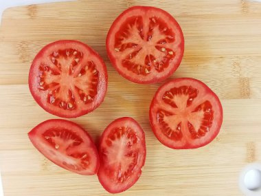 Tahta kesme tahtasına yerleştirilmiş dilimlenmiş olgun domateslerin üst görüntüsü. Doğal dokuya sahip taze kırmızı sebze dilimleri, sağlıklı yiyecekler ve yemek malzemeleri konsepti. Temiz kırsal gıda geçmişi, insan yok..