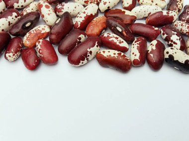 Benekli kırmızı ve beyaz kuru fasulyeler beyaz arka planda üst kenar boyunca sıralanmış. Fotokopi alanı, sağlıklı beslenme ve tarım kavramına sahip en az gıda arkaplanı.