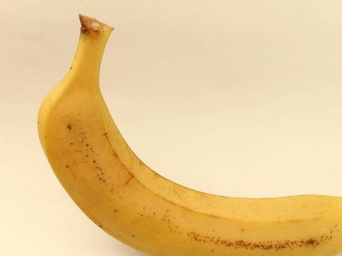 Hafif pastel arka planda izole edilmiş tek bir olgun muz. Tasarım, ambalaj, reklamcılık, sağlıklı beslenme, tropikal meyve ve doğal ürün için kopyalama alanı olan minimal gıda kavramı.