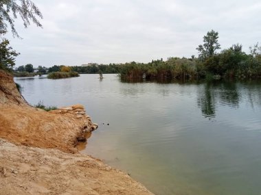 Kumlu sahil ve yeşil bitki örtüsüyle sakin göl manzarası geniş. Huzurlu atmosferi ve yumuşak renkleri olan doğal doğa manzarası..