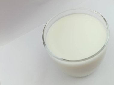 Yukarıdan temiz beyaz arka planda çekilmiş bir bardak taze süt. Fotokopi alanı olan minimalist gıda konsepti. Doğal süt ürünleri, sağlıklı beslenme, kahvaltı ve yaşam tarzı teması.
