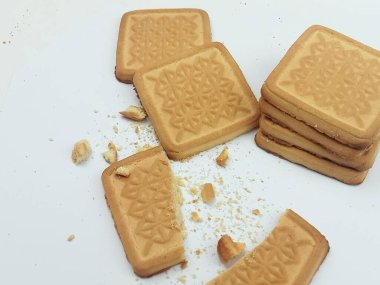 Kırık tereyağlı kurabiyeler ve beyaz arka plana saçılmış kırıntılar. Abur cubur konseptini, yeme sürecini ve ev yapımı tatlı fikrini gösteren sıradan bir besin. Gıda blogları, makaleler, sosyal medya ve aşçılık illüstrasyonları için uygun.