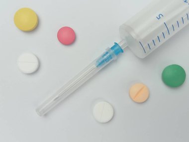 Beyaz arka planda şırınga ve renkli haplar içeren sağlık sigortası konsepti. Eğitim, tasarım ve bilgi içeriği için kopyalama alanı olan tıbbi ve ilaç teması.