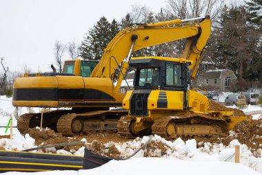 Sarı bir inşaat alanında traktör ve kazıcı.