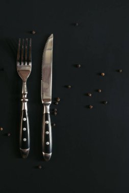 Siyah zemin üzerinde bir çatal ve bıçak ve biraz da karabiber.