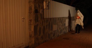 Hayalet kılığına girmiş biri Cadılar Bayramı 'nda elinde balkabağıyla sokakta yürür.