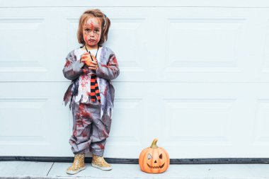 Cadılar Bayramı 'nı Jack O Lantern' in yanındaki garaj kapısında zombi gibi giyinmiş bir kız kutluyor.