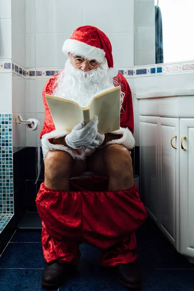 Noel Baba banyoda, tuvalette oturuyor, sıçıyor, kitap okuyor.
