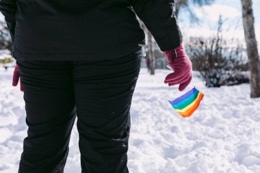 Karlı bir bölgede elinde gökkuşağı bayrağı tutan lezbiyen bir kadının arkasında.