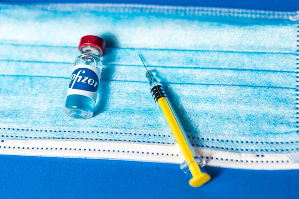 MADRID, SPAIN - JAN, 25, 2021: Pfizer şirketinin amblemi ile dolu, mavi arka planda cerrahi maske ve şırınga.