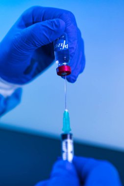 MADRID, SPAIN - JAN, 25, 2021: Doktor şırınganın şırıngasını COVID-19 aşı şirketi Pfizer 'ın aşılamak için şişeye sokuyor. Coronavirus aşısı konsepti