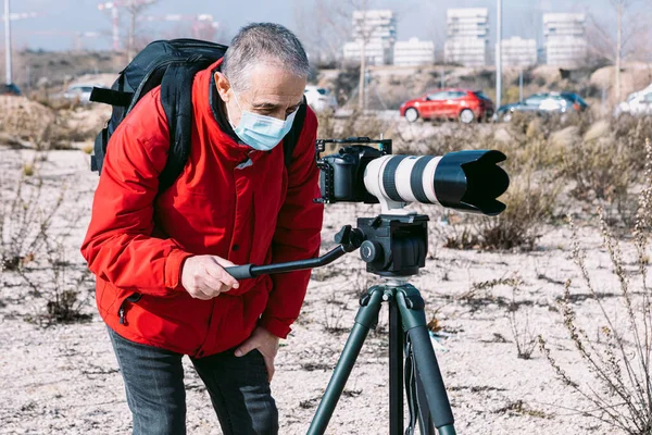 Cerrahi maske takan bir fotoğrafçı sokakta tripod kullanarak fotoğraf ve video çekiyor.
