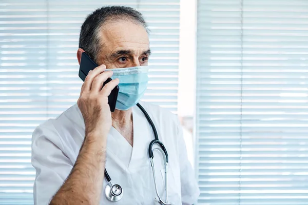 Reifer Männlicher Arzt Krankenschwester Mit Gesichtsmaske Telefonierend Neben Einem Krankenhausfenster — Stockfoto