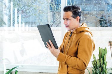 Gülümseyen adam, yeşil çiçekler ve bitkilerle çevrili bir tablete bakıyor.