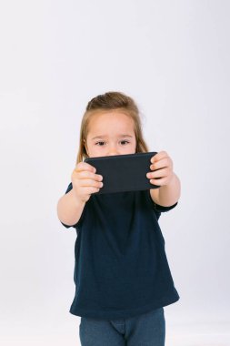 Elinde cep telefonu olan küçük sarışın kız oyun oynuyor.