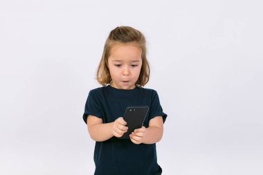 Elinde cep telefonuyla el kol hareketi yapan küçük sarışın kız.