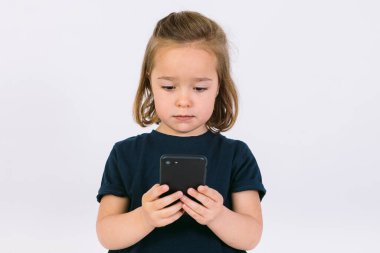 Küçük sarışın kız cep telefonuna bakıyor.