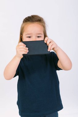 Elinde cep telefonu olan küçük sarışın kız oyun oynuyor.