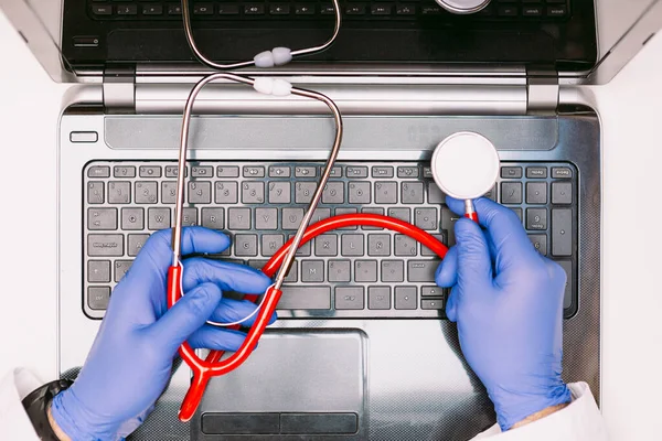 Aerial view of a laptop and doctor\'s hands with latex gloves holding a stethoscope