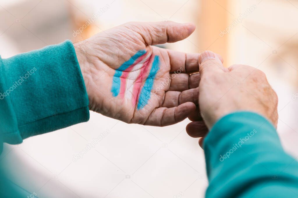 Transsexual man rests his hands with the transsexual flag painted on them, on a railing