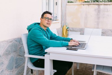 Genç bir adam evinin bahçesinde bilgisayarına yazarak telgraf çekiyor.