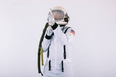 Uzay giysisi ve miğferli erkek kozmonot, beyaz arka planda, gökyüzünü işaret ediyor..