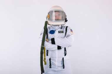 Uzay giysisi ve miğferli erkek kozmonot, kolları çapraz, beyaz arka planda.