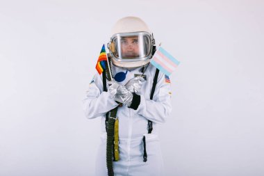 Beyaz arka planda lgtbi gökkuşağı bayrağı taşıyan, uzay giysisi ve kasklı eşcinsel erkek kozmonot..