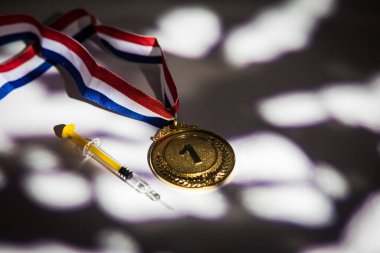 Şampiyonun altın madalyası ve içinde ışık ve gölgeler olan doping maddesi olan şırıngası pencereden içeri giriyor. Spor ve doping kavramı