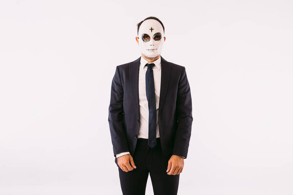 Мужчина в костюме и галстуке, в маске убийцы с крестом на лбу на Хэллоуин. Карнавал и празднование Хэллоуина