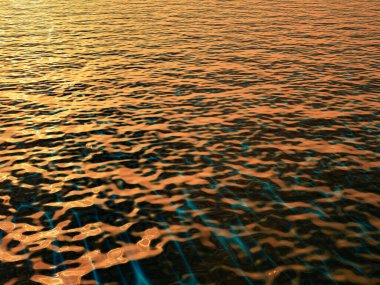 Gün batımında pürüzsüz deniz yüzeyinden yansıyan ılık altın renkler