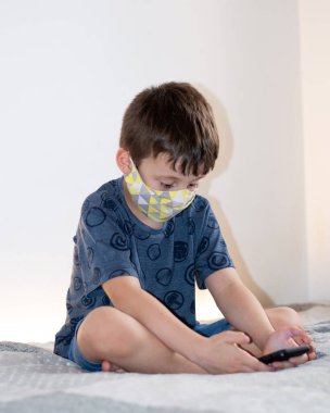 Yüz maskesi takan akıllı telefon kullanan genç bir çocuk.