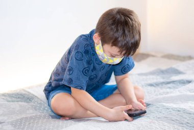 Yüz maskesi takan akıllı telefon kullanan genç bir çocuk.