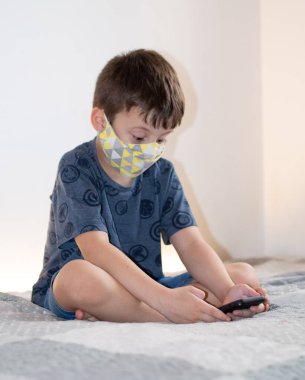 Yüz maskesi takan akıllı telefon kullanan genç bir çocuk.