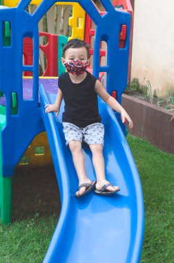 Çocuk çocuk oyun parkında maske takıp kayıyor.